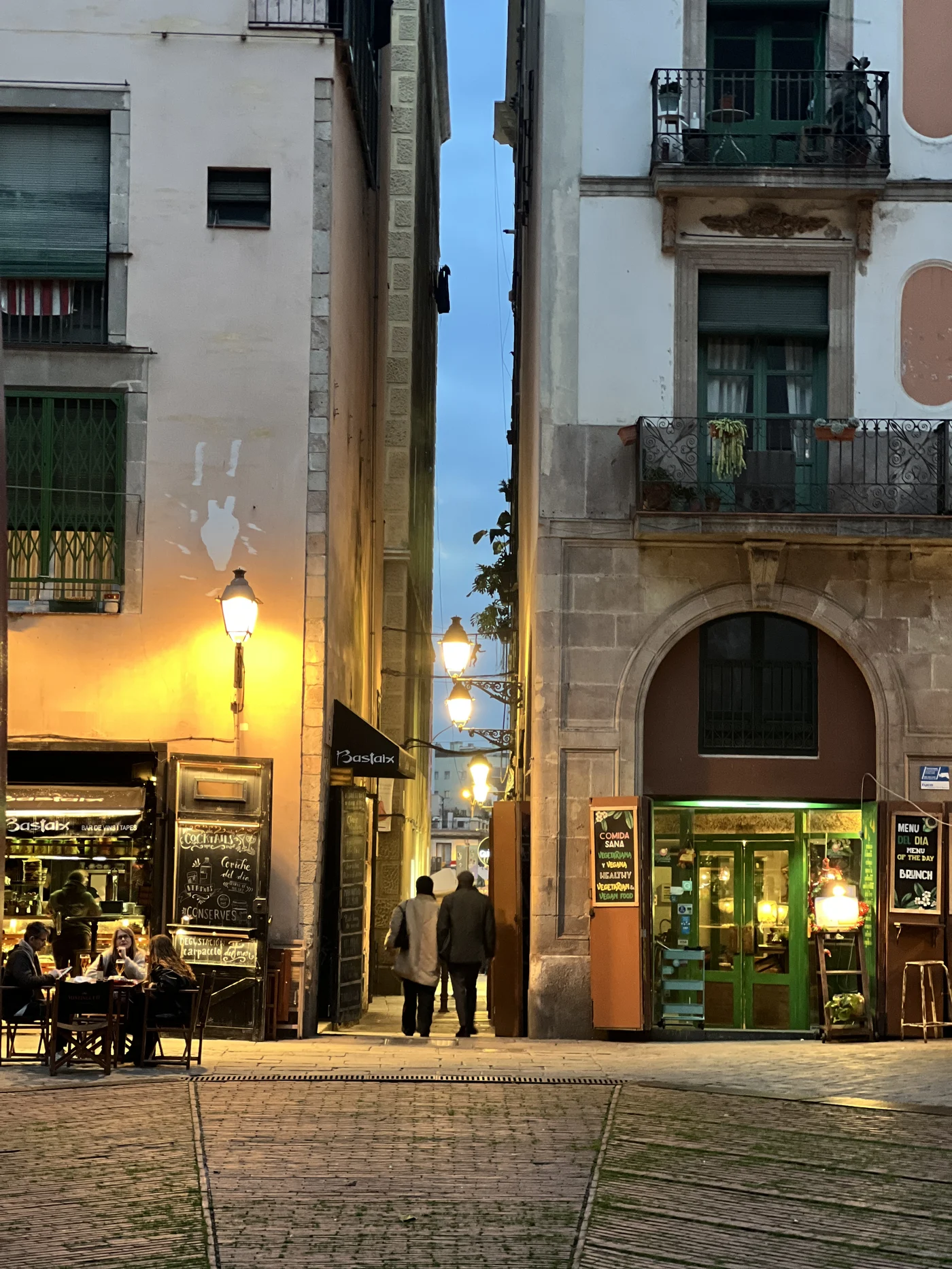 A narrow Barri Gòtic lane at dusk, lantern-lit with tapas bars and diners