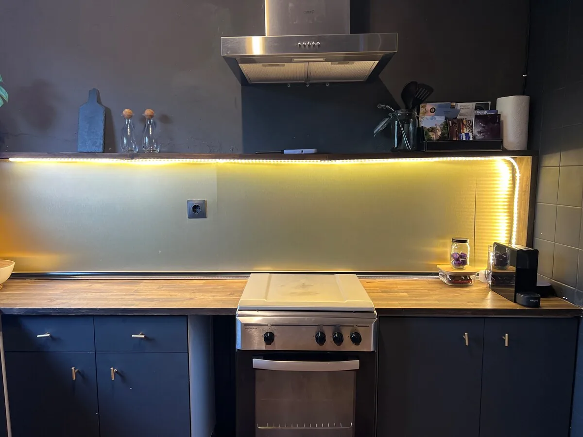 Kitchen with a stove, extractor hood, LED-lit backsplash and deep navy cabinets