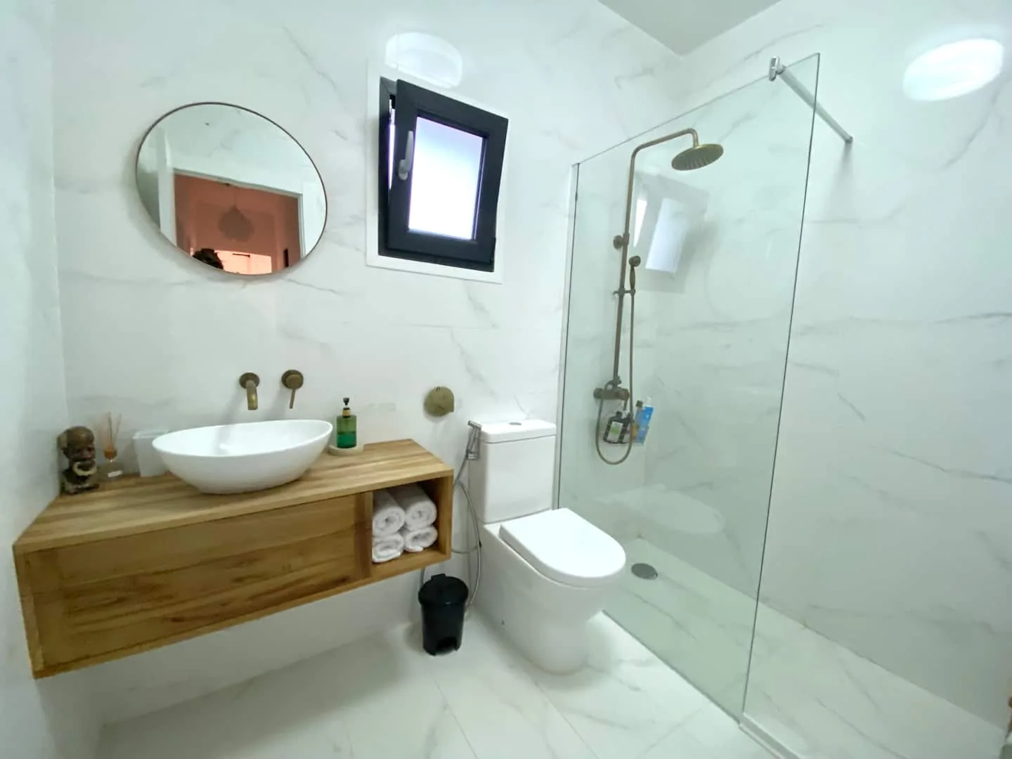Bathroom with marble tiling, a walk-in rain shower, wood vanity and round mirror