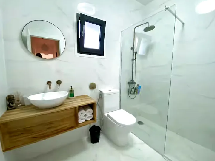 Bathroom with a wood vanity, vessel sink, toilet and a walk-in rain shower in marble tiling