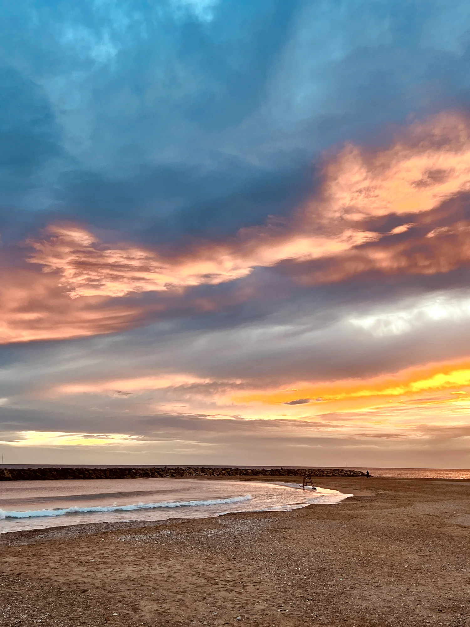 Pastel pink and blue sunset over the curved bay and breakwater near the beach