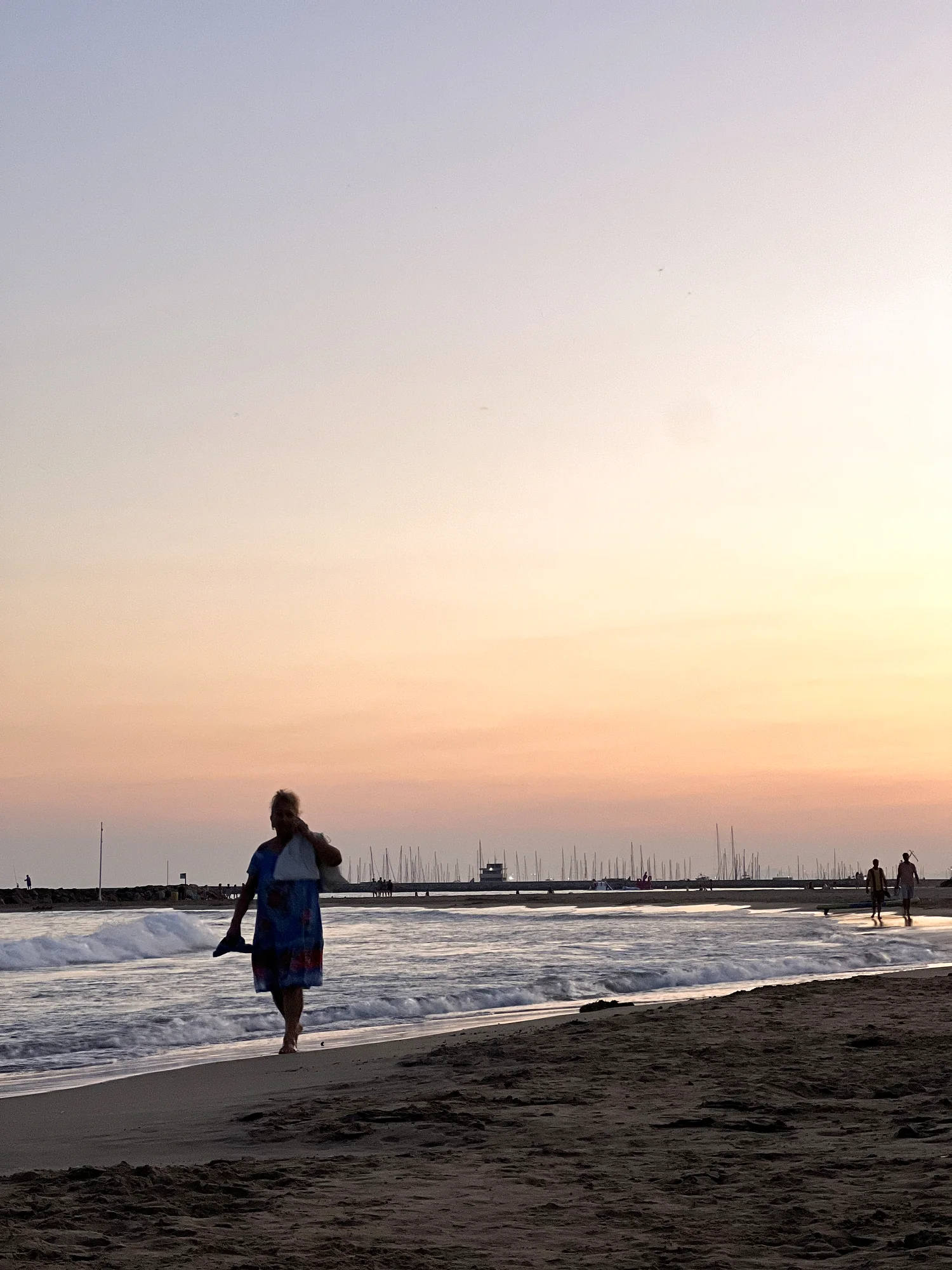 A person walking the tideline at sunset along the beach
