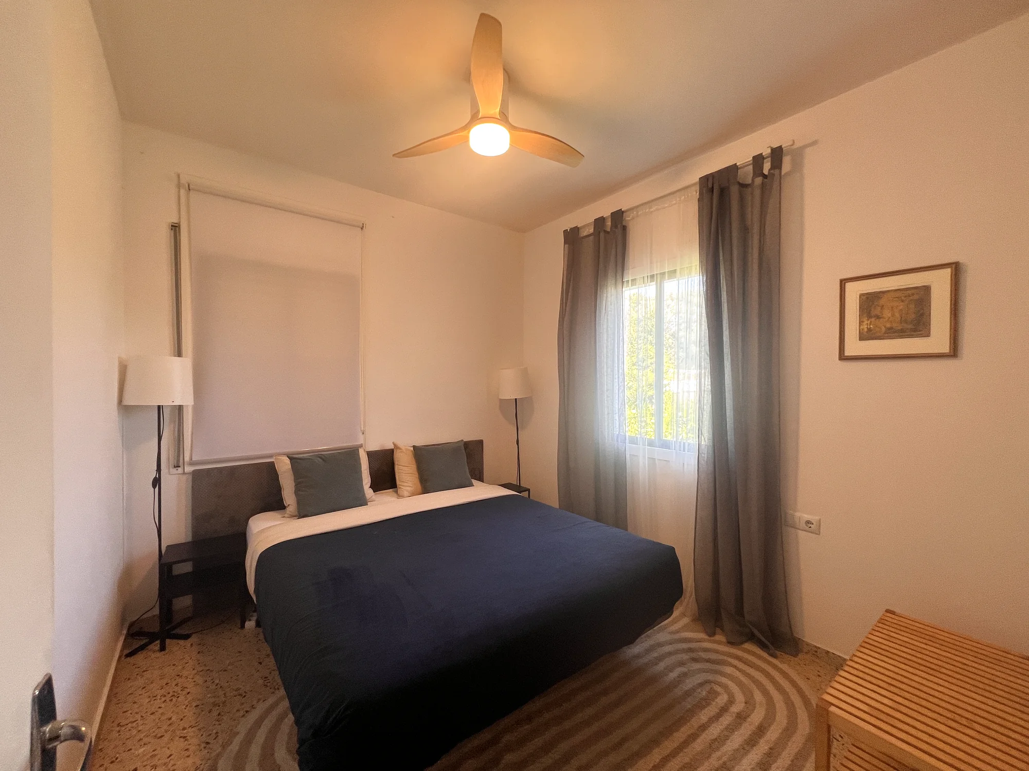 Double bedroom with a deep navy duvet, teal and gold pillows, twin bedside lamps and framed art