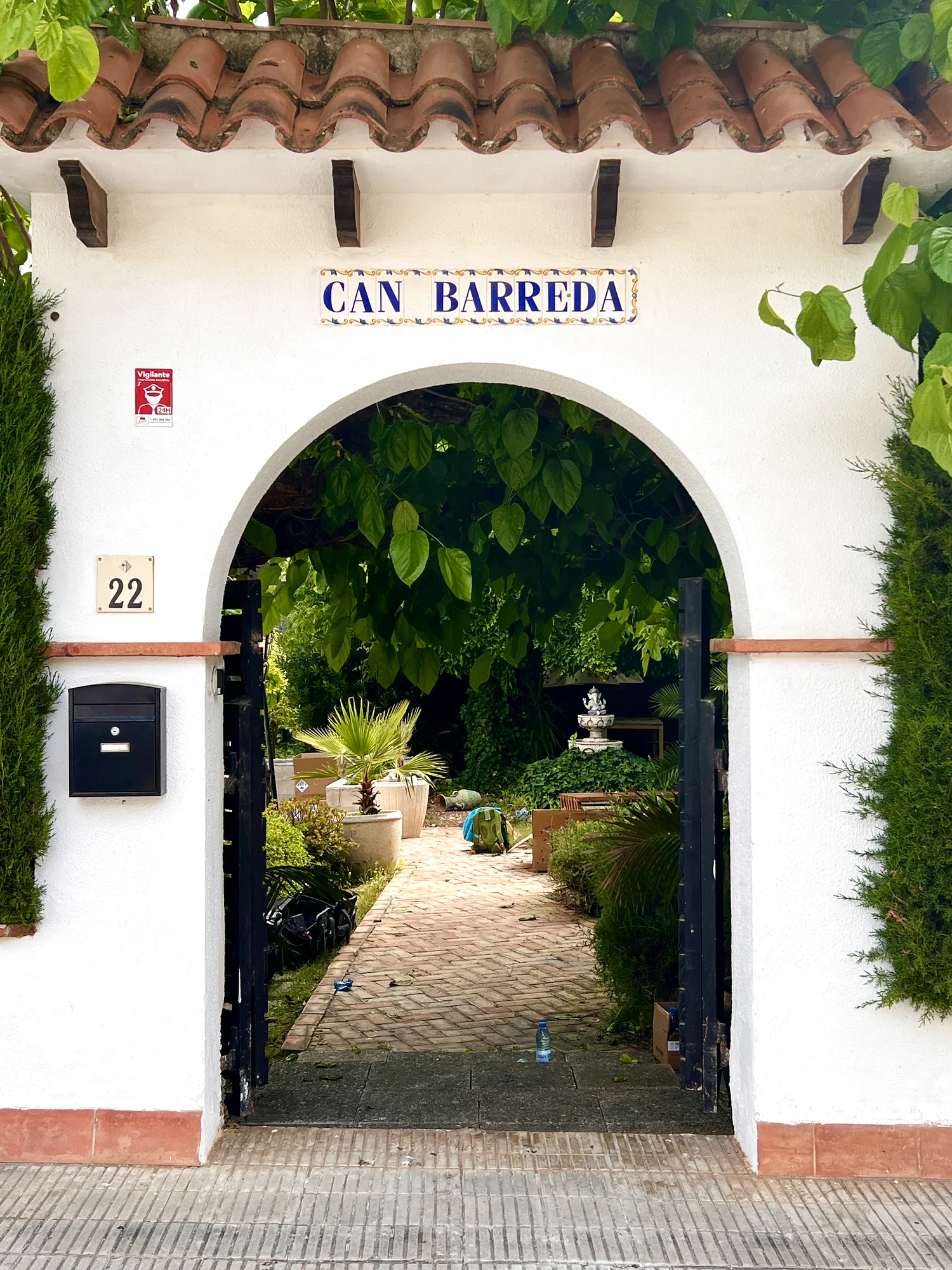 Arched white entrance gate reading Can Barreda, house number 22, framed by greenery