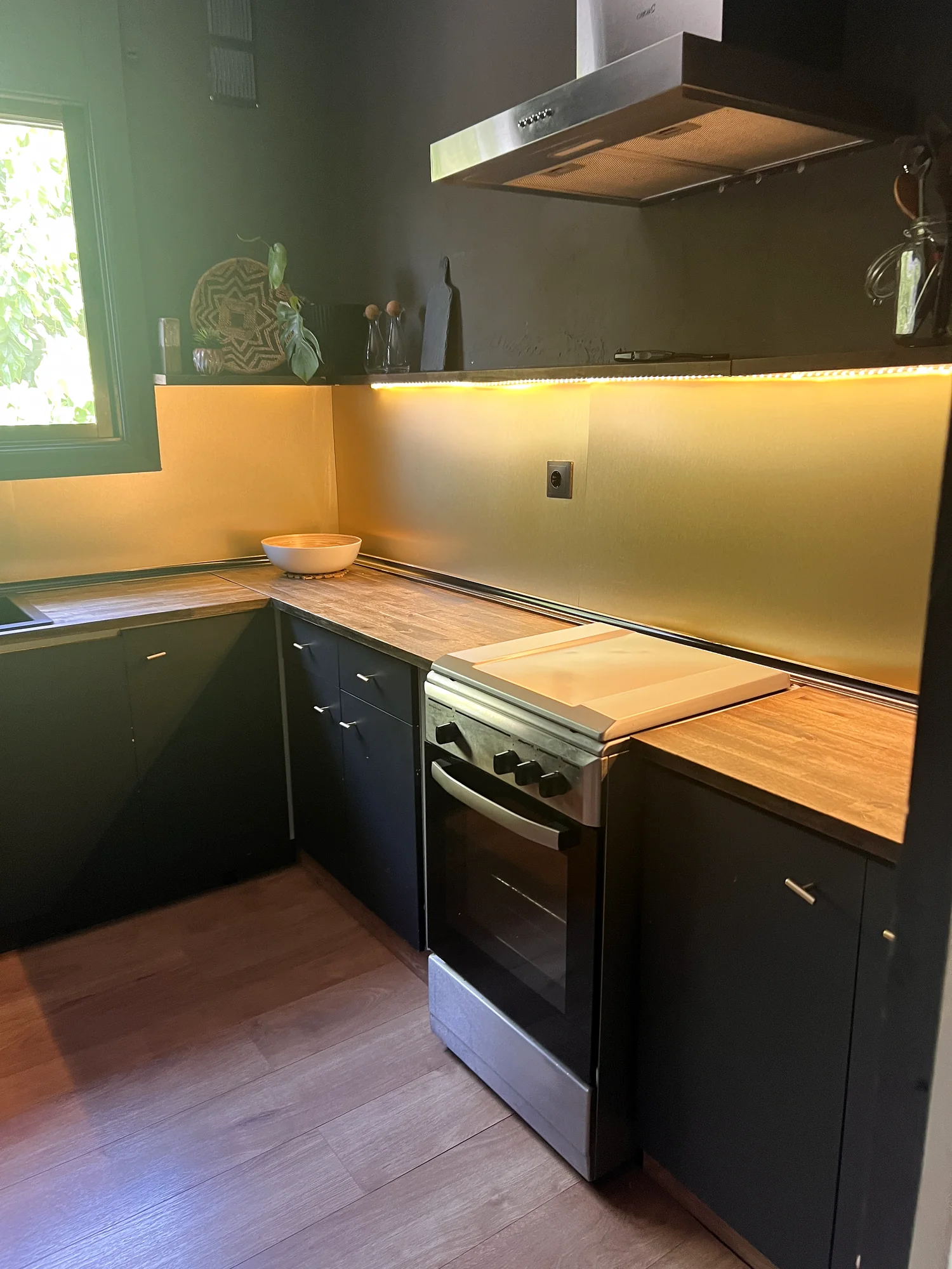 Kitchen with navy cabinets, a wood worktop, oven, extractor hood and an LED-lit backsplash by the window