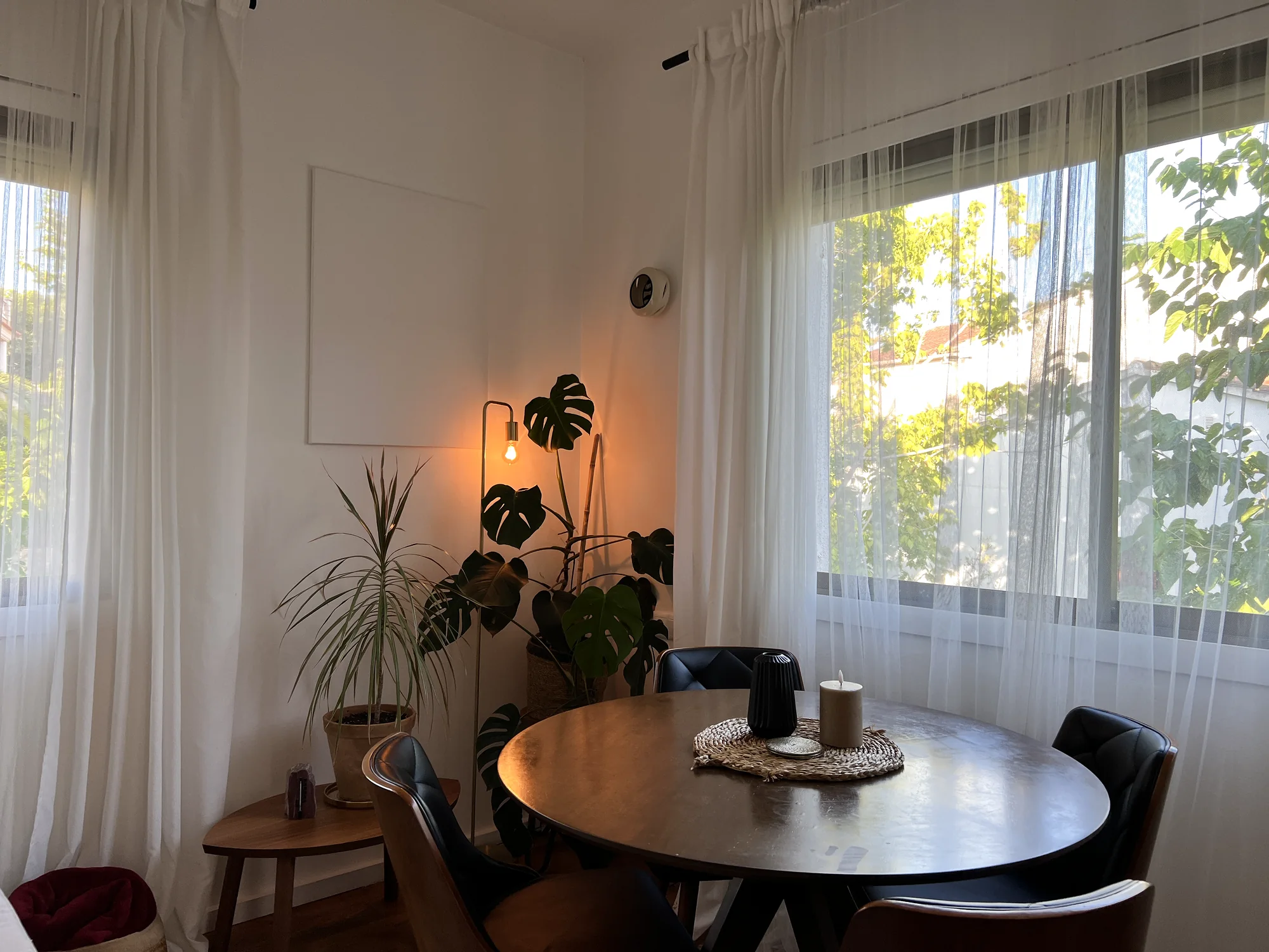 Cosy dining corner at dusk with a round table, leather chairs and plants lit by a warm floor lamp