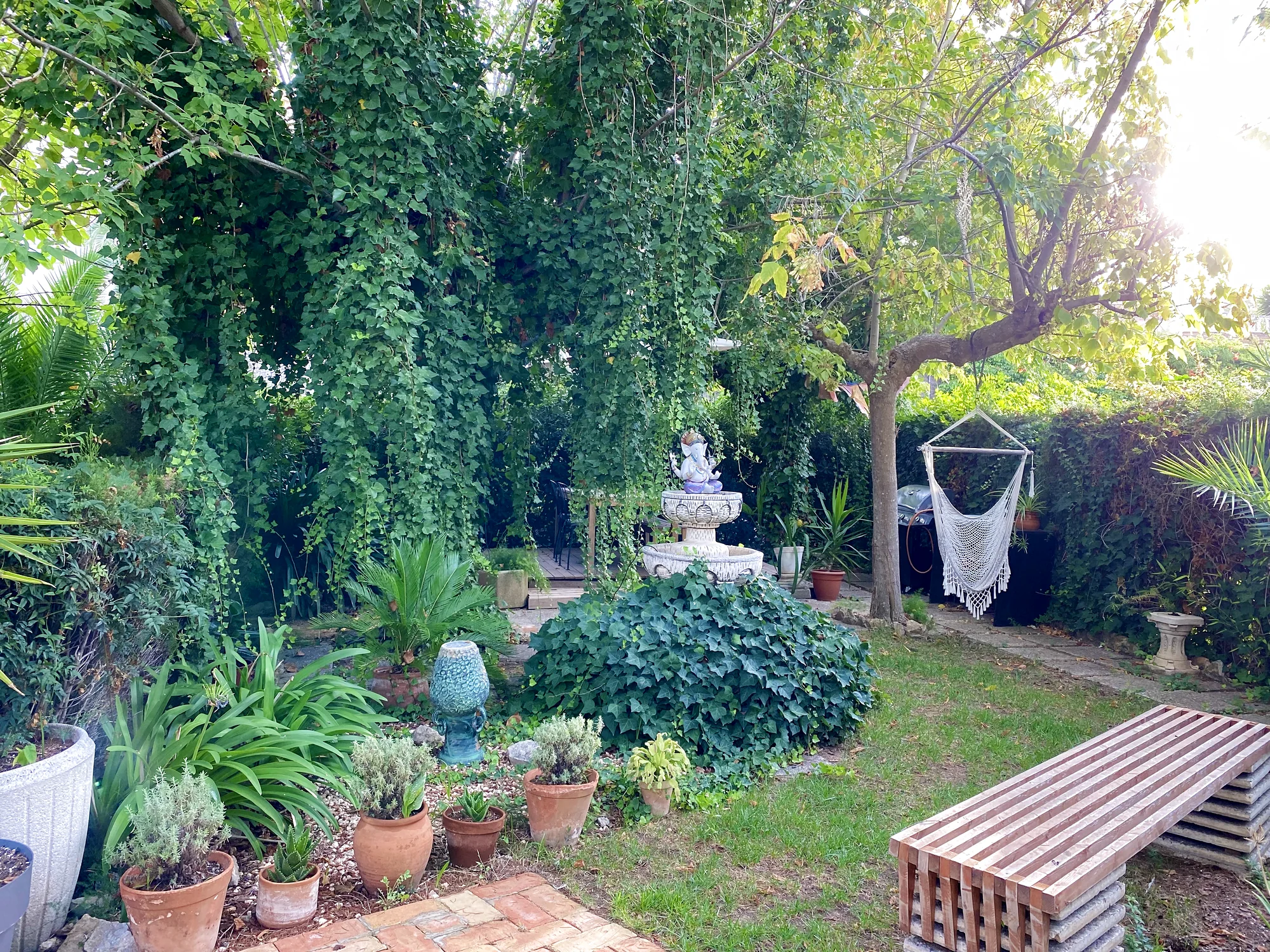 Lush garden with a stone fountain, a hanging hammock chair and potted flowers
